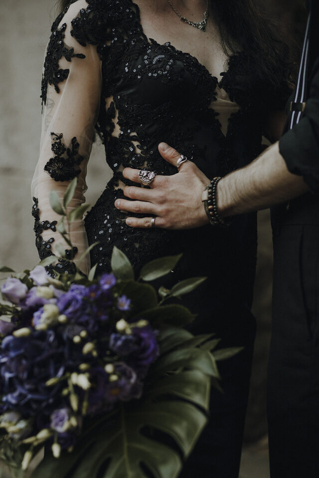 Nahaufnahme eines Gothic-Brautkleids mit Spitzenärmeln und violettem Brautstrauß – Metal Me vereint dunkle Eleganz und alternative Hochzeitsträume für Hell Yes! Weddings