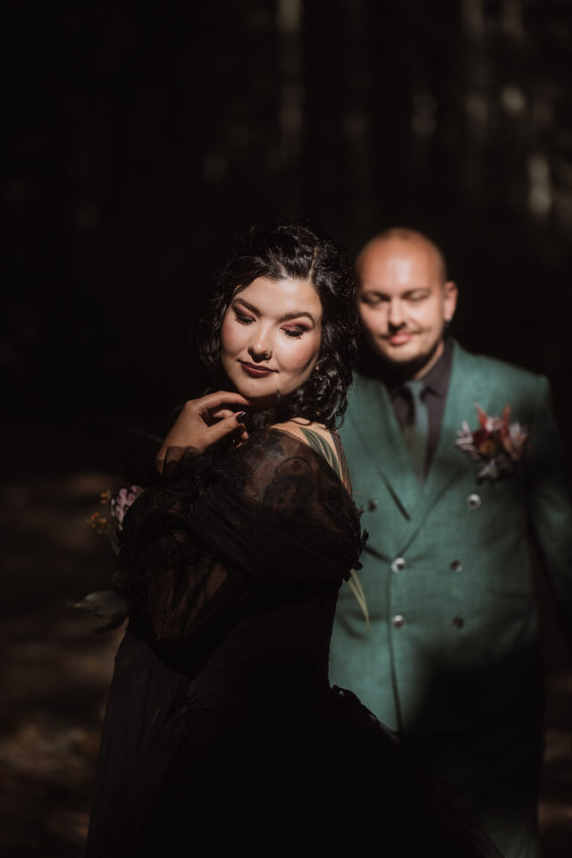 Spotlight auf’s schwarze Brautkleid: Braut im Fokus, Bräutigam weich im Hintergrund – moody Portrait von Patricia Bakker (alternative Hochzeit).