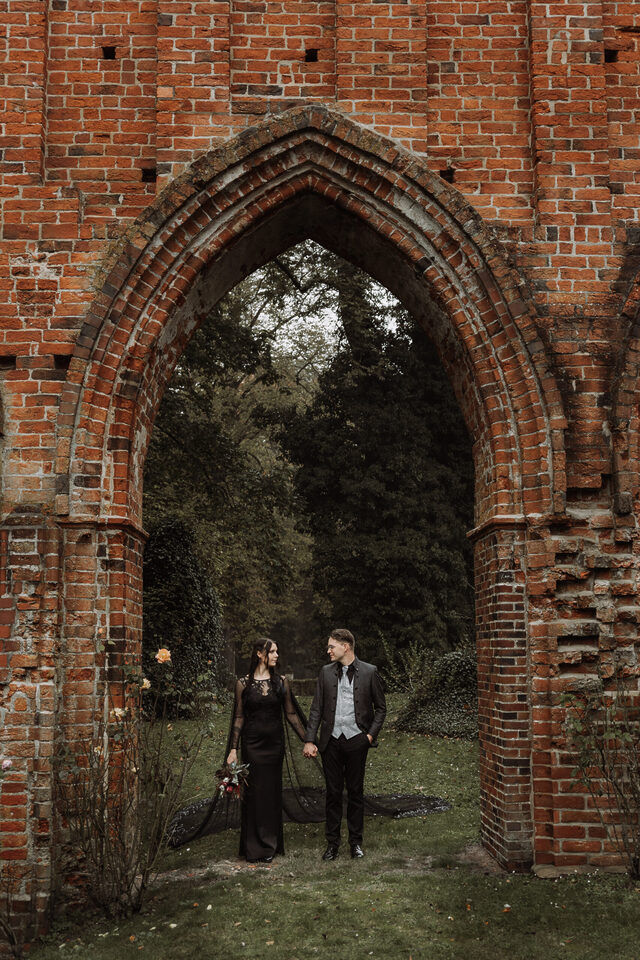 Hochzeitspaar unter gotischem Backsteinbogen – dramatisches Paarfoto bei Ruinenkulisse, perfekt für deine alternative Hochzeit.