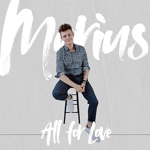 Marius Pokutta, Hochzeitsmaler aus NRW, sitzt auf einem Hocker vor hellem Hintergrund mit Schriftzug „All for Love“.