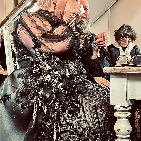 Heiratende Person in schwarzem Hochzeitsoutfit mit schwarzem Blumenstrauß und dramatischen Tülldetails