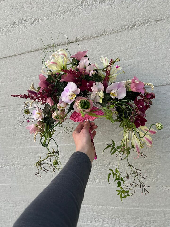 Locker gebundener Brautstrauß in Rosa, Bordeaux und Creme mit Orchideen und langen grünen Ranken