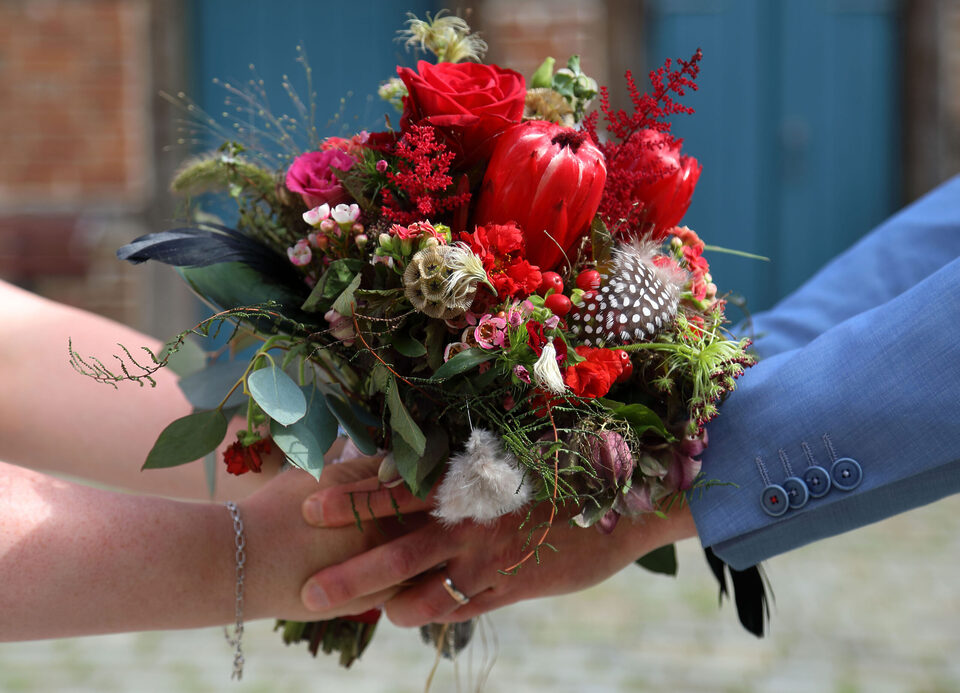 Üppiger roter Brautstrauß mit Rosen, Protea, Beeren, Grün und auffälligen gefleckten Federn