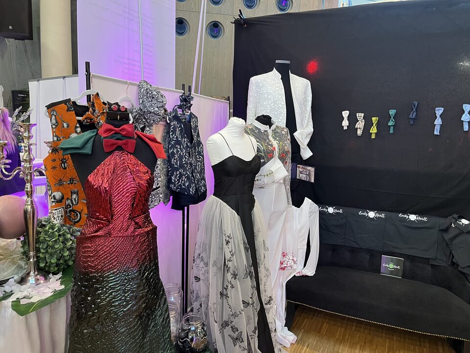 Messestand von Lucky Hardt mit maßgeschneiderter Hochzeitsmode, Kleidern, Anzügen und bunten Accessoires