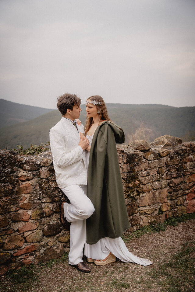 Hochzeitspaar in maßgeschneiderter Hochzeitsmode von Lucky Hardt vor einer alten Steinmauer