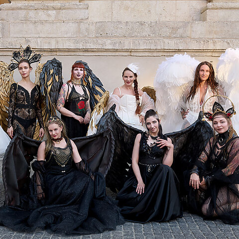 Gruppe in schwarzen und weißen Hochzeitsoutfits mit großen Flügeln und auffälligem Kopfschmuck