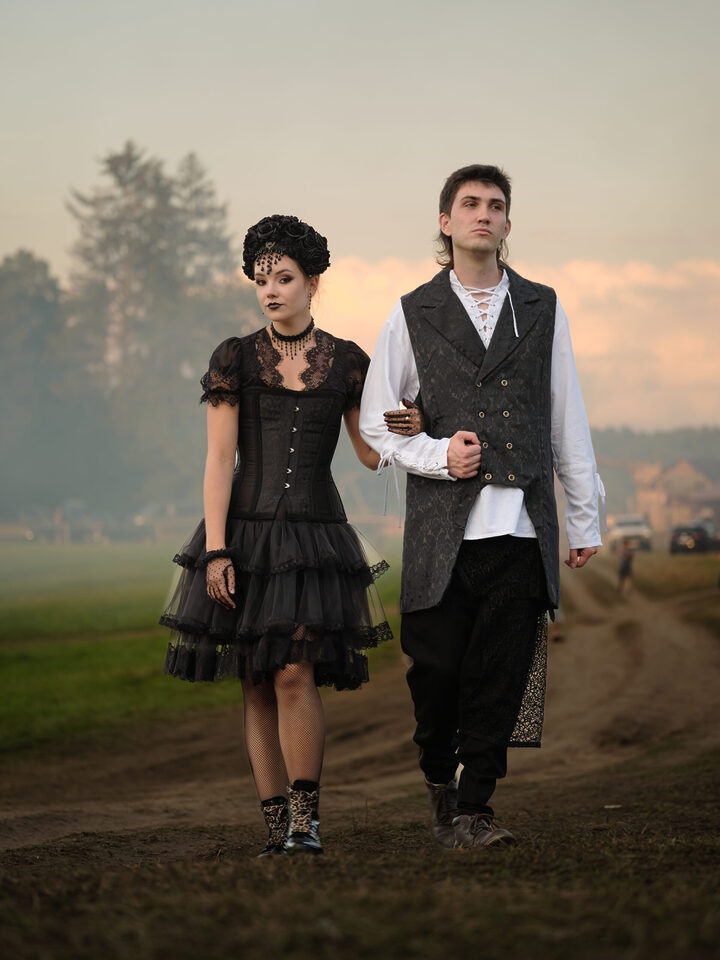 Zwei Personen im Abendlicht, eine im kurzen schwarzen Kleid, die andere mit hellem Hemd, dunkler Weste und Hose