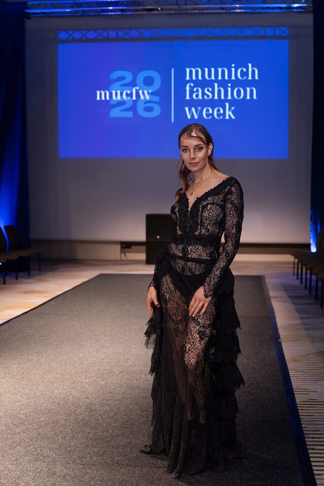 Person im schwarzen Spitzenkleid auf einem Laufsteg vor dem Schriftzug Munich Fashion Week