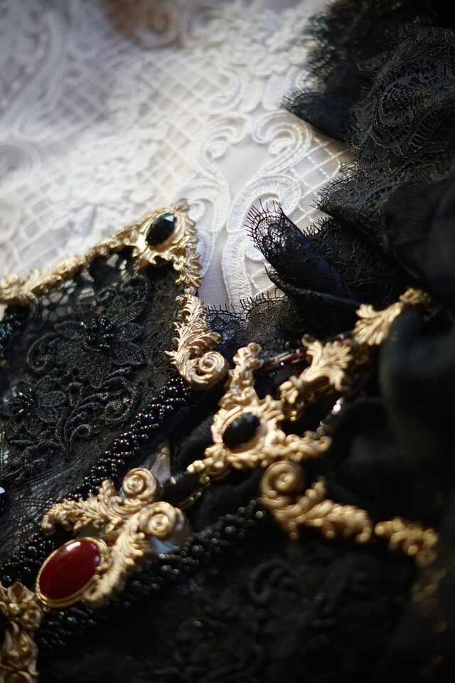 Schwarze und weiße Spitze mit goldfarbenen Schmuckelementen sowie roten und dunklen Schmucksteinen