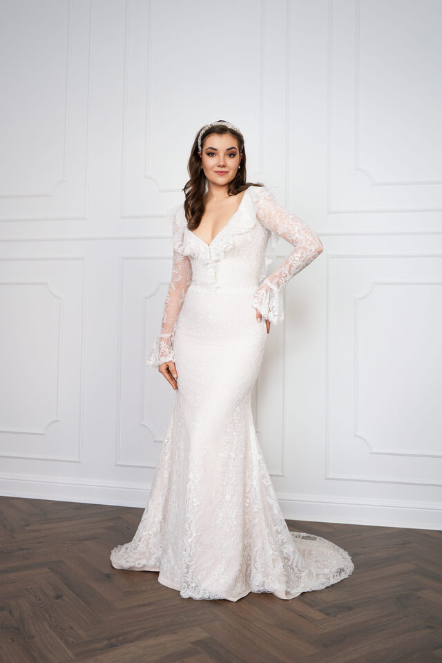 Person in langem weißem Spitzenkleid mit transparenten Ärmeln, schmaler Silhouette und ausgestelltem Saum