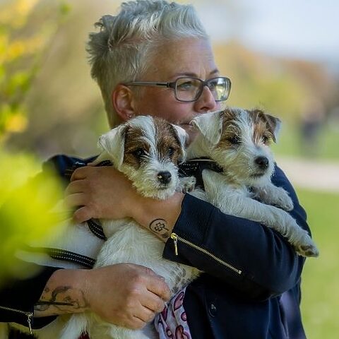 Tanja Rauth hält zwei kleine Terrier auf dem Arm und blickt seitlich aus dem Bild.