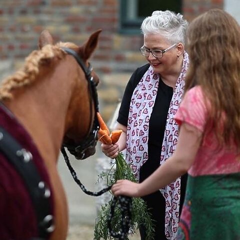 Traurednerin Tanja Rauth steht bei einer Hochzeitszeremonie neben einem Pferd und reicht ihm eine Karotte.